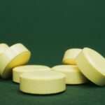 A close-up of scattered yellow tablets on a green surface, emphasizing their color and shape.