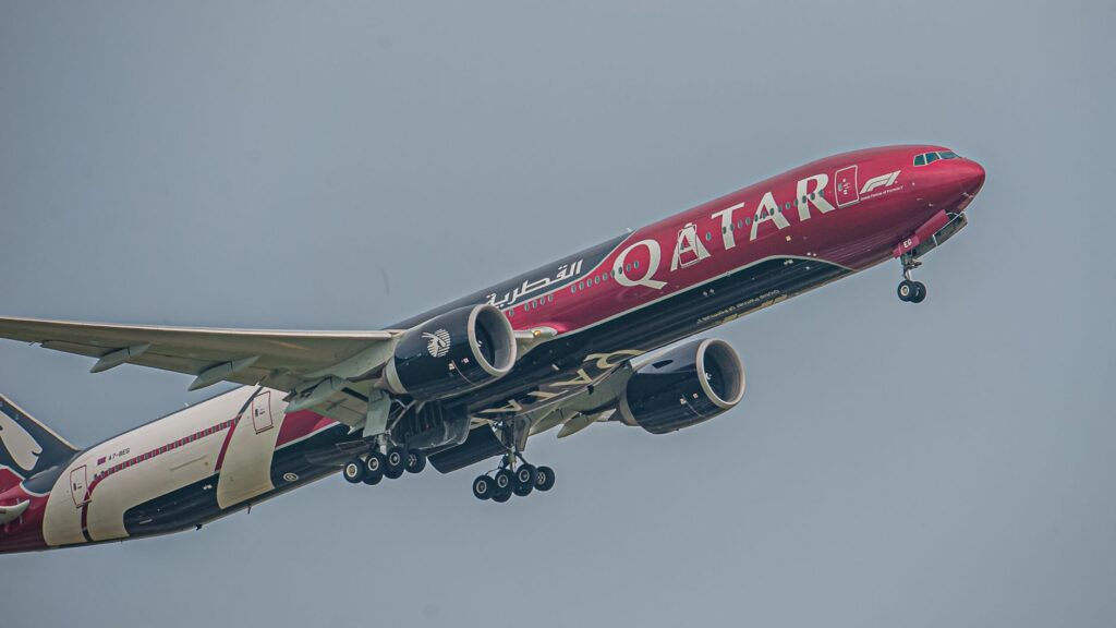 A Qatar Airways plane featuring F1 branding captured mid-flight against a clear sky.