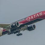 A Qatar Airways plane featuring F1 branding captured mid-flight against a clear sky.
