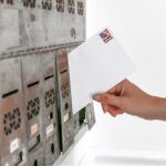 Close-up of a hand inserting a stamped envelope into a mailbox, symbolizing voting.