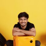 Smiling young man in casual wear posing with colorful props indoors, radiating positivity and joy.