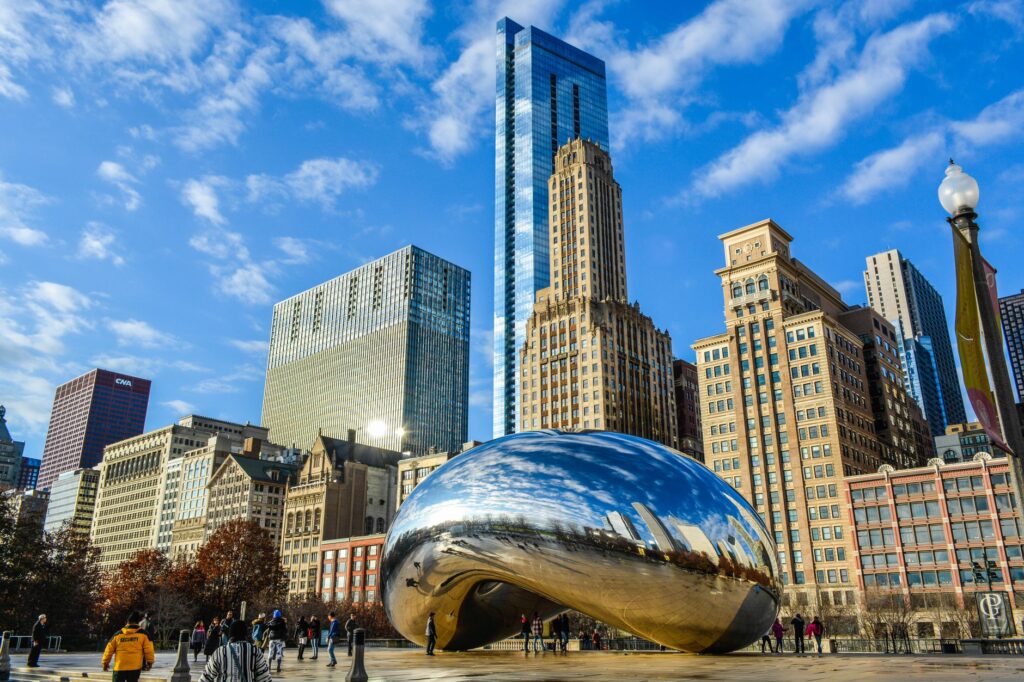 View of the iconic Cloud Gate sculpture in Chicago's Millennium Park with city skyscrapers in the background.