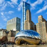 View of the iconic Cloud Gate sculpture in Chicago's Millennium Park with city skyscrapers in the background.