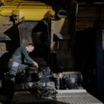 Mechanic inspecting engine in dimly lit garage. Industrial setting with repair focus.