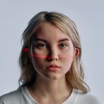 Close-up of a young woman with facial recognition lasers projected, symbolizing future technology.