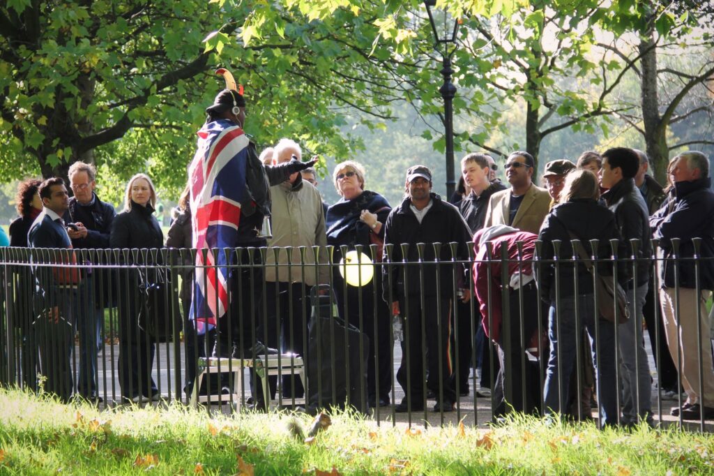 A lively gathering at Hyde Park's Speakers' Corner with a speaker draped in the Union Jack flag.