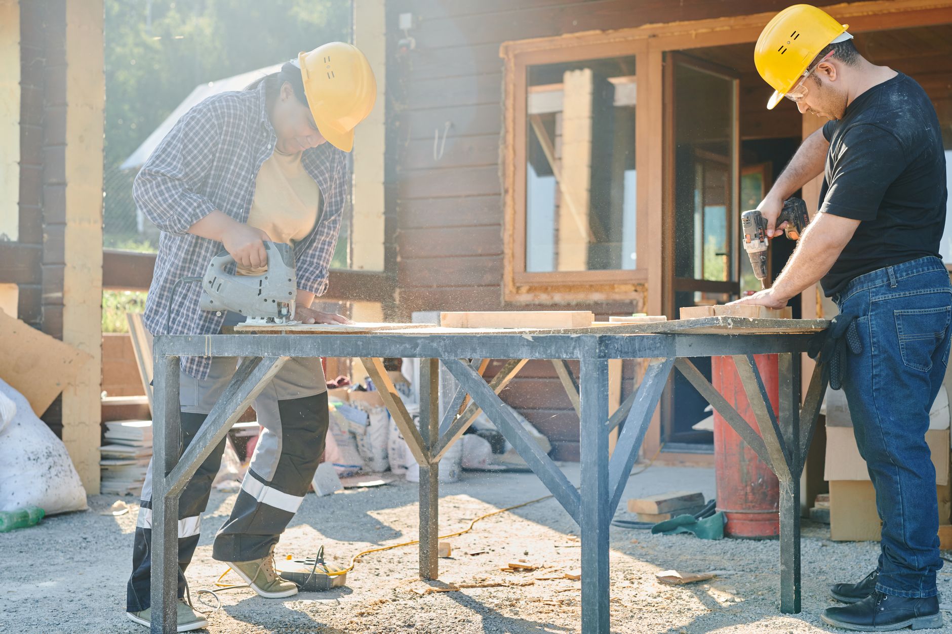 Two construction workers using power tools on a sunny day.