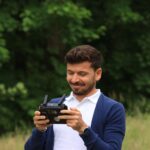 Smiling man using drone controller outdoors in a lush green setting.