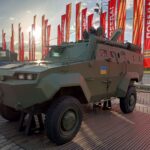 An armored military vehicle showcased outside with flags and sunlight in Moscow.