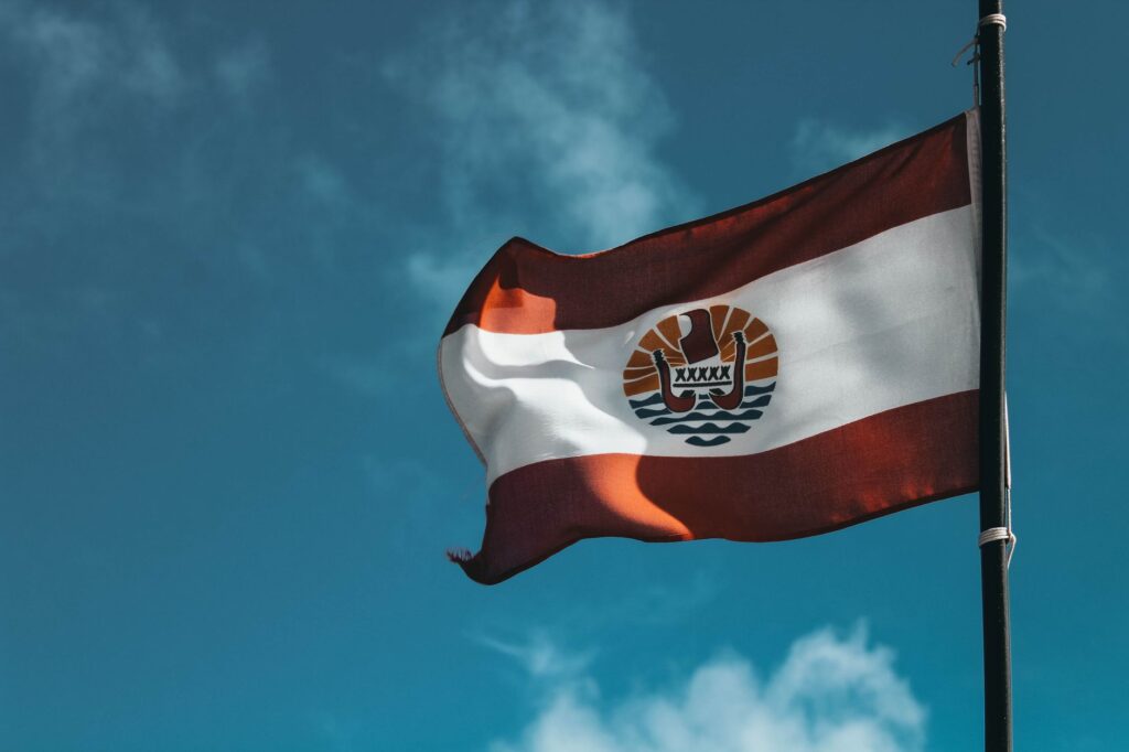 Dynamic view of the French Polynesia flag waving against a vibrant blue sky.
