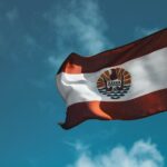 Dynamic view of the French Polynesia flag waving against a vibrant blue sky.