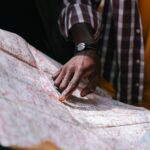 Close-up of a hand pointing at a detailed map, outdoors, wearing a striped shirt.