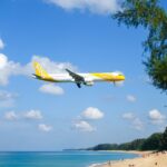 Commercial airplane landing over a beautiful beach in Phuket, Thailand with clear skies.