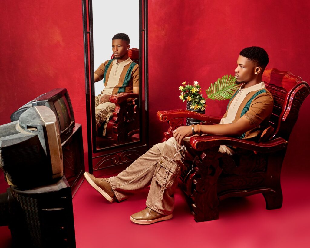 Fashionable young man sitting in front of a mirror against a vivid red backdrop, showcasing style and elegance.