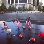 A poignant tribute at the 9/11 Memorial in NYC with flags and flowers honoring victims.