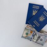Top view of two Ukrainian passports with US dollar bills on a white surface.
