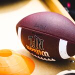 An American football placed on a training bench next to an orange training cone, ideal for sports concept.