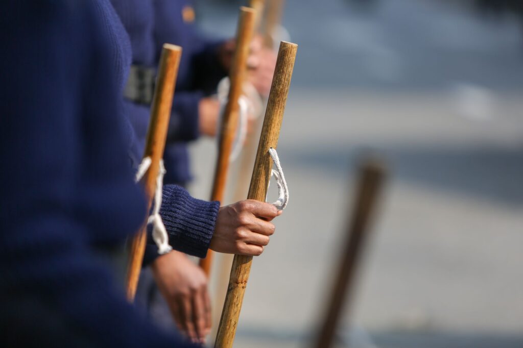 Close-up view of military personnel holding wooden sticks during a parade, focused on hands and uniforms.
