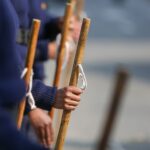 Close-up view of military personnel holding wooden sticks during a parade, focused on hands and uniforms.