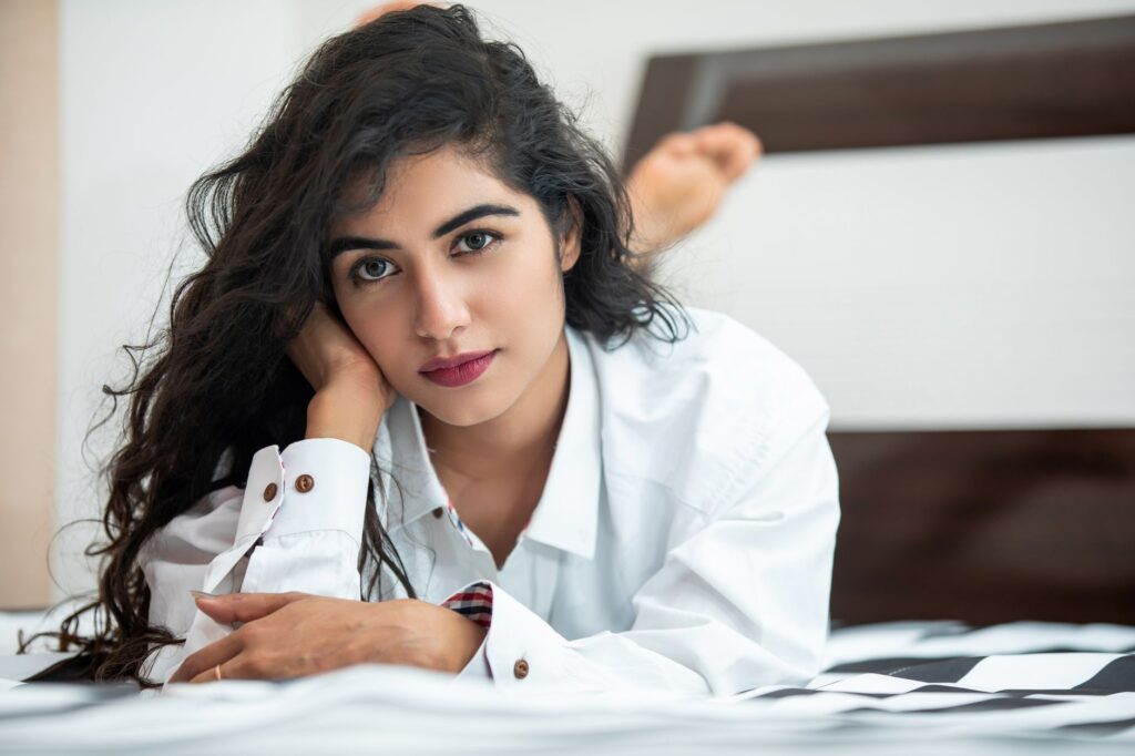 Portrait of a young woman with long hair relaxing on a bed in a white shirt.