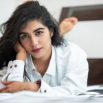 Portrait of a young woman with long hair relaxing on a bed in a white shirt.