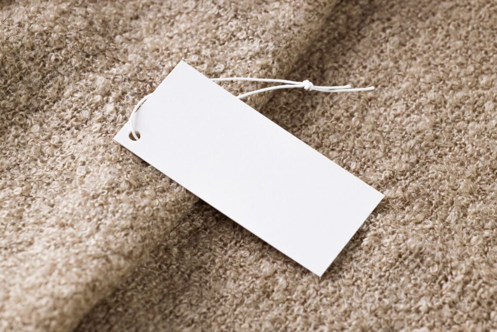Close-up of a blank white price tag on textured beige fabric, ideal for branding use.