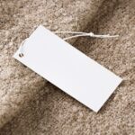 Close-up of a blank white price tag on textured beige fabric, ideal for branding use.