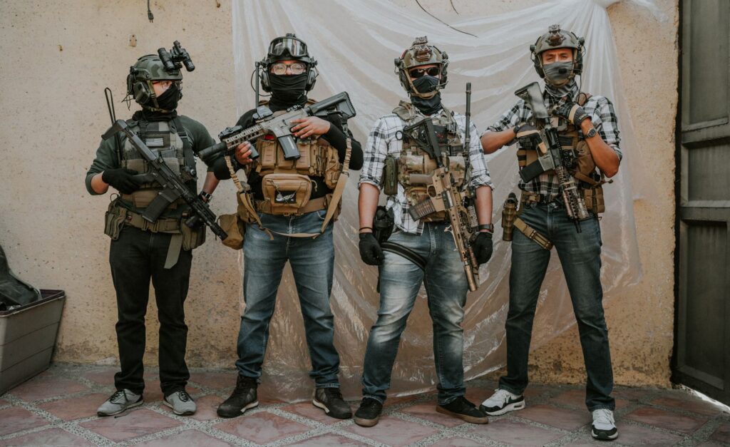 Four adults in tactical gear and masks pose indoors. Modern military theme.
