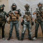 Four adults in tactical gear and masks pose indoors. Modern military theme.