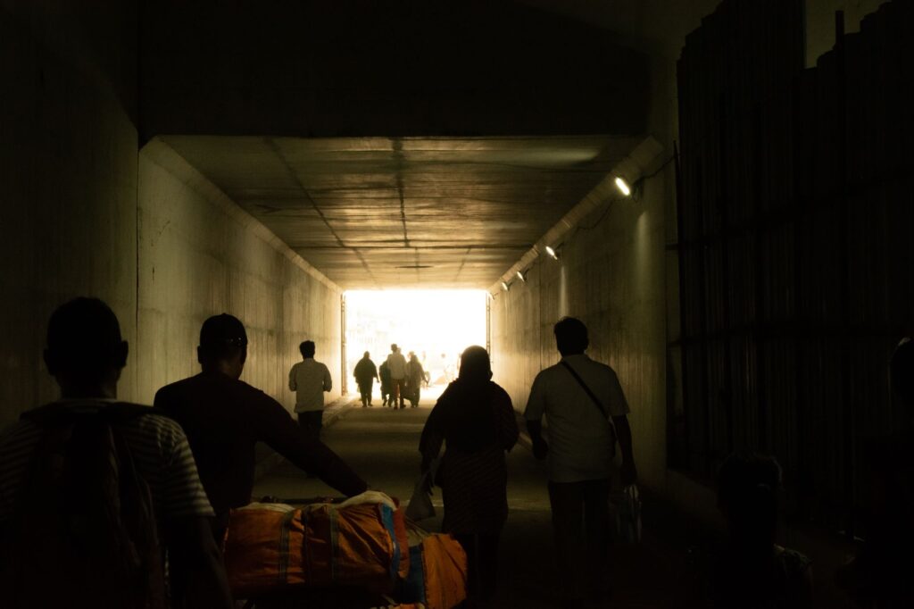 Silhouetted people walking through a tunnel leading to a bright exit in Tamil Nadu, India.