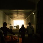 Silhouetted people walking through a tunnel leading to a bright exit in Tamil Nadu, India.