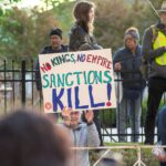 Protesters gather in Towson with signs against sanctions, advocating for peace and justice.