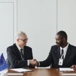 Corporate handshake between diverse businessmen representing EU and US flags, symbolizing partnership and collaboration.
