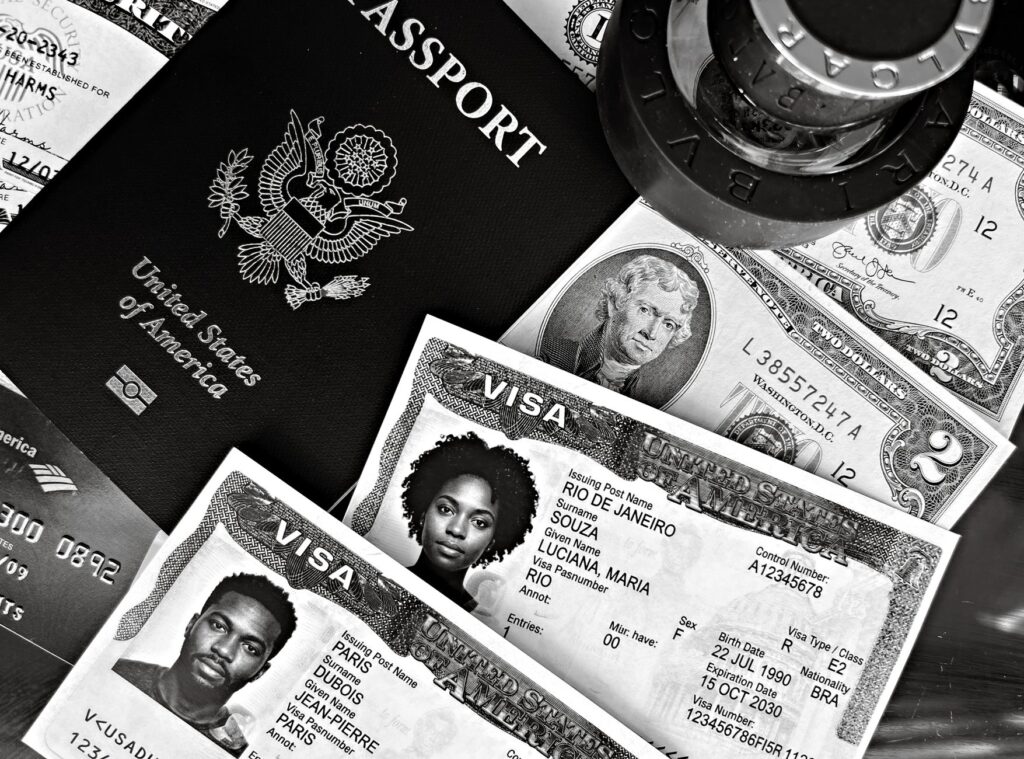 A black and white composition of a US passport, visas, and currency, showcasing travel essentials.