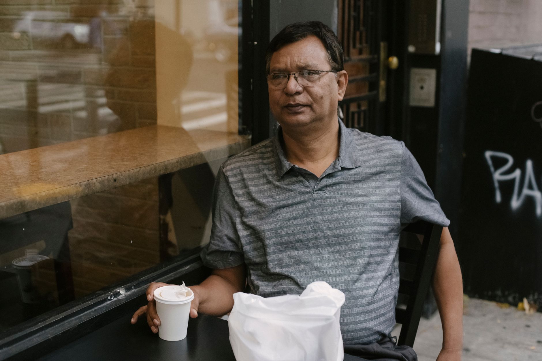 Concentrated Asian male in eyeglasses sitting near window at table with cup of hot drink in outdoor cafe during break