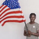 A young man proudly holding the US flag in a studio. Promotes patriotism and civic engagement.