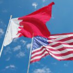 Flags of Bahrain and the United States waving against a bright blue sky, symbolizing international relations.