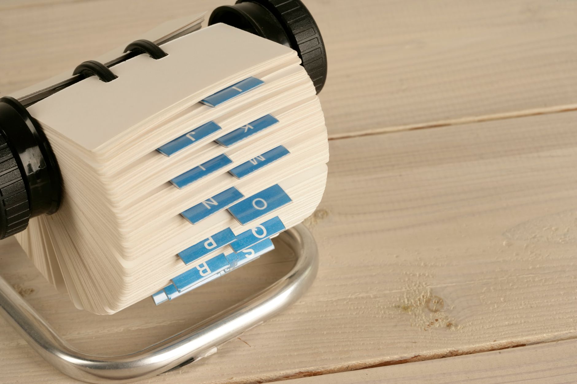 A close-up of a traditional Rolodex with alphabet tabs on a wooden desk.