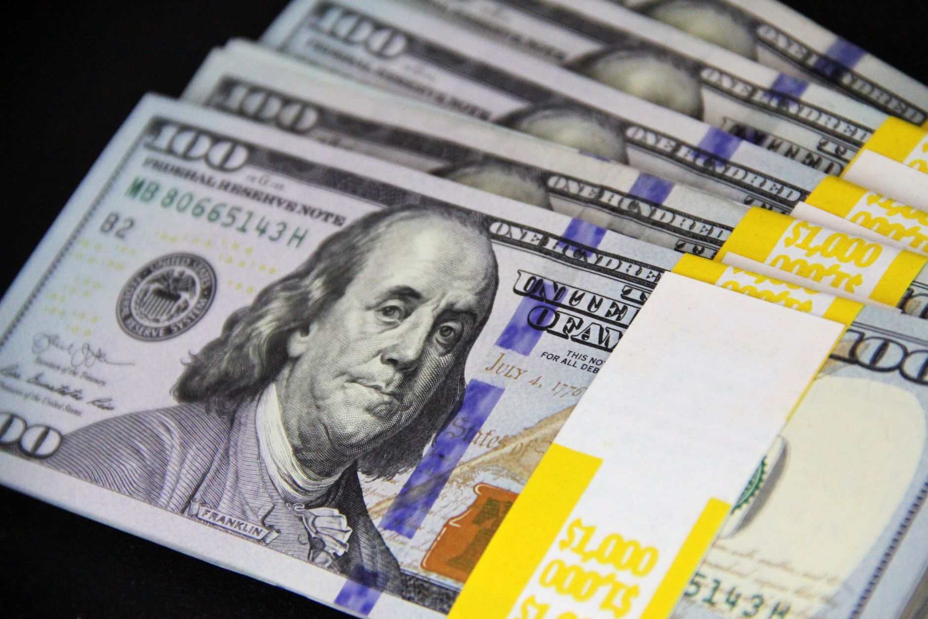 Close-up of stacked US hundred dollar bills on black surface, emphasizing wealth and finance.