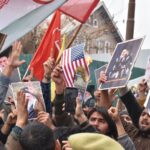 Crowd of demonstrators holding flags and banners during a protest outdoors.