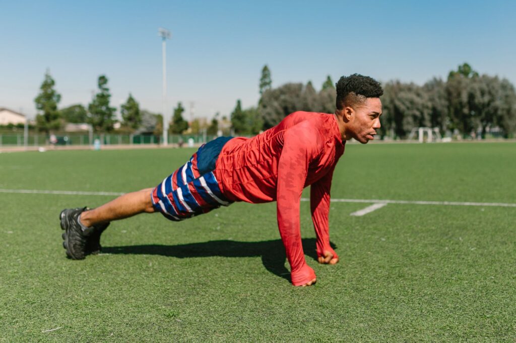 Athletic man doing push-ups on a sunny sports field, capturing outdoor fitness.