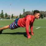 Athletic man doing push-ups on a sunny sports field, capturing outdoor fitness.