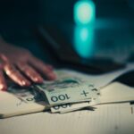 Close-up of hand reaching for banknotes on an office desk with a notebook and calculator.