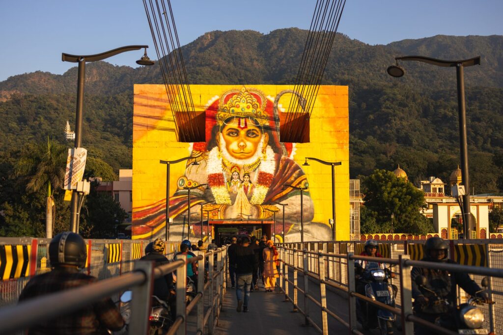 Vibrant Hanuman mural on a bridge in Rishikesh, Uttarakhand, with people and mountain backdrop.