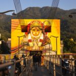 Vibrant Hanuman mural on a bridge in Rishikesh, Uttarakhand, with people and mountain backdrop.