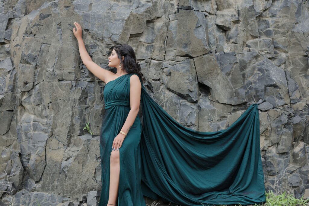 A woman in a flowing green dress poses against a rugged rock wall, exuding elegance and natural beauty.