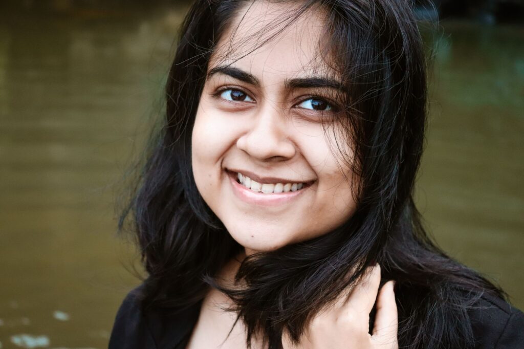 Close-up portrait of a woman smiling with black hair, captured outdoors by the water.