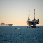 Offshore oil platform with container ship in tranquil sea during daytime.