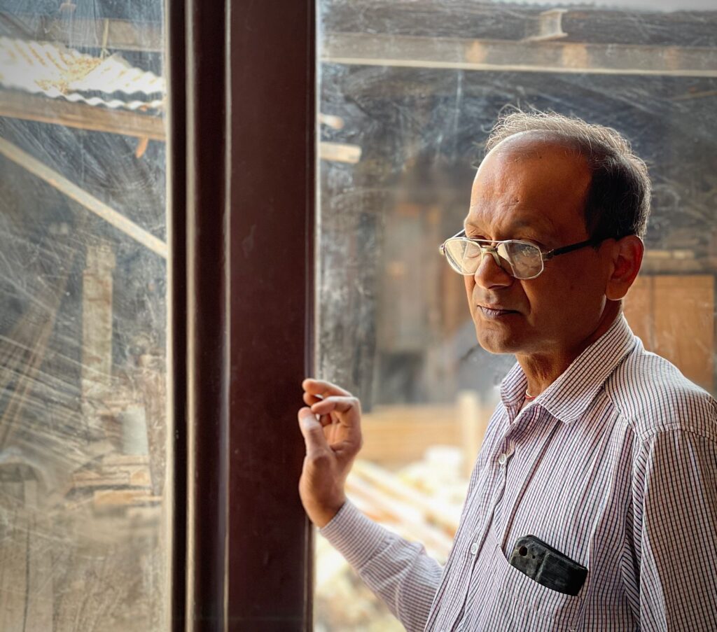 A thoughtful man wearing eyeglasses stands by a glass window, looking outside.