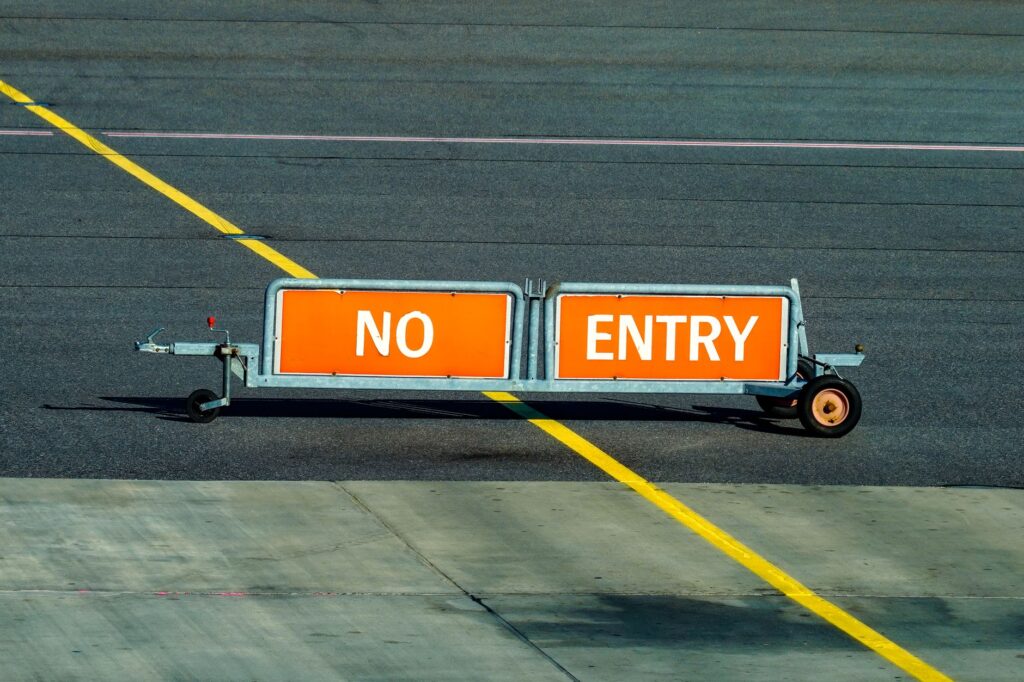 A warning sign indicating no entry on an airport taxiway with a bold yellow line.